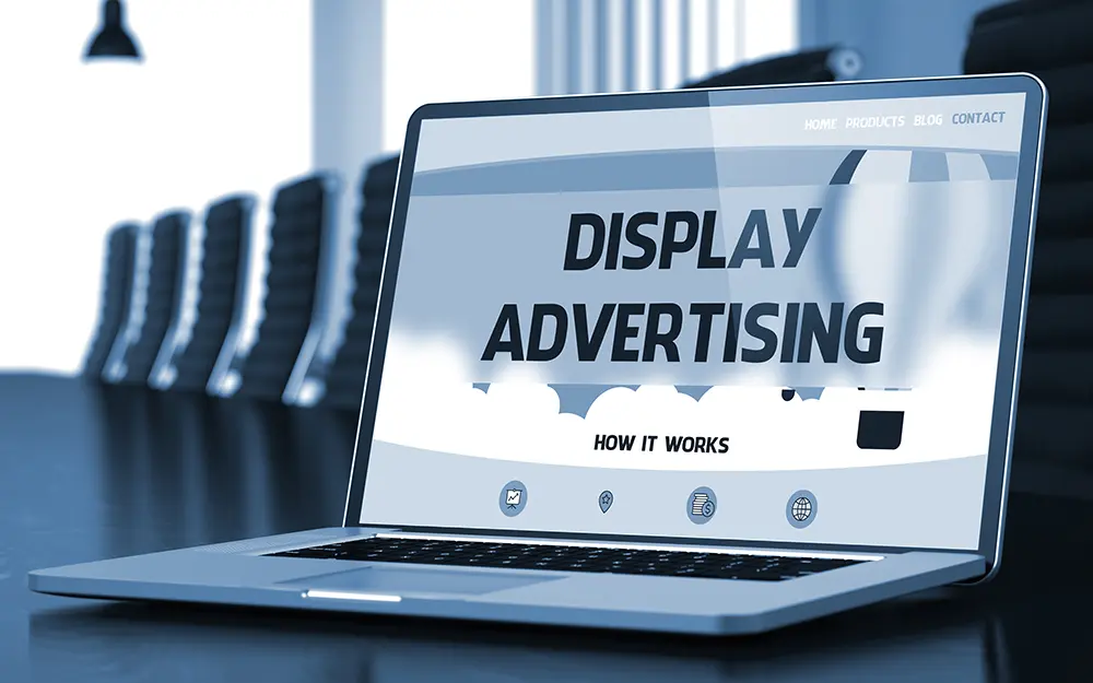 Blue-toned photo of a laptop on a boardroom table showing a landing page headlined "Display Advertising" with the subhead "How It Works"