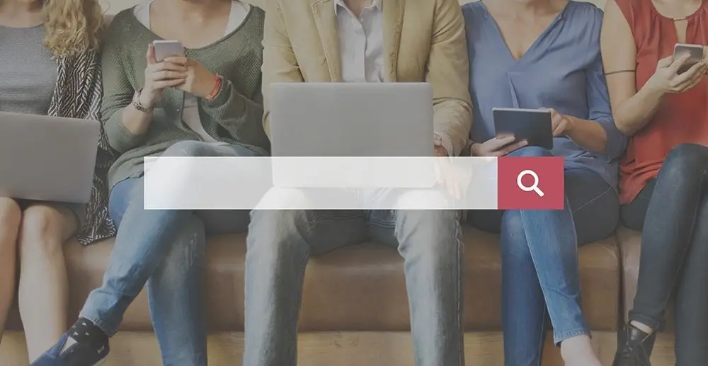 Five people seated on a bench using phones, a laptop and a tablet, with a large white search bar and red magnifying glass button across them