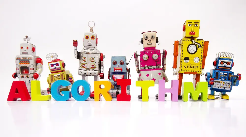 Row of colorful vintage tin toy robots standing behind wooden block letters spelling "Algorithm" on a white background