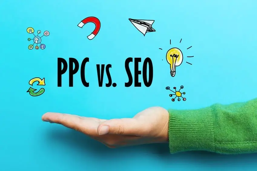 Open upturned palm in a green sweater beneath hand-drawn text "PPC vs. SEO" with doodled magnet, paper plane and lightbulb icons on turquoise