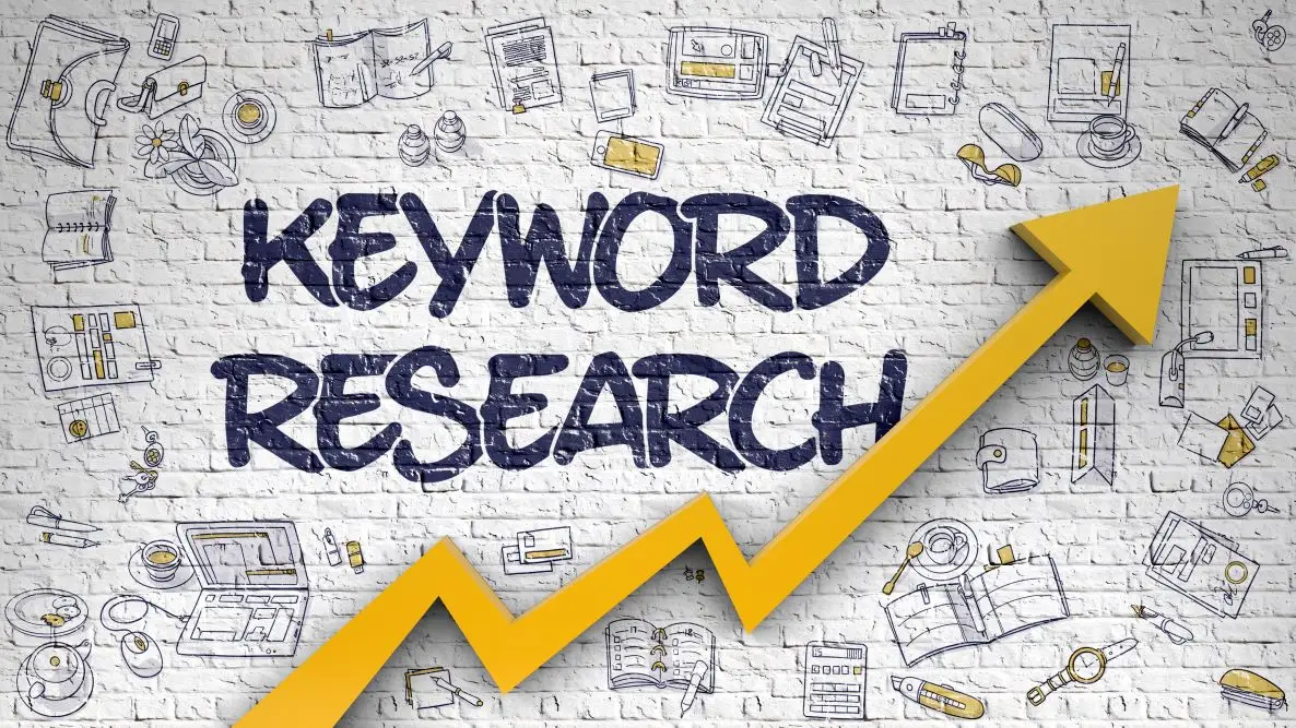 "KEYWORD RESEARCH" painted on a white brick wall beside a rising yellow arrow, framed by hand-drawn doodles of laptops, books and coffee cups.