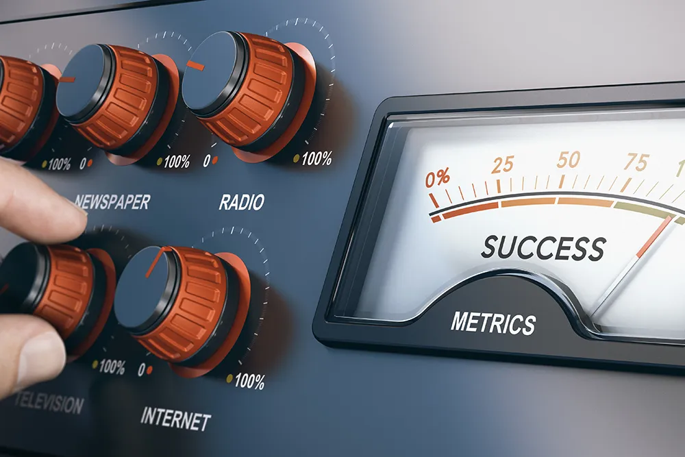 Fingers turning dials labeled Newspaper, Radio, Television and Internet on a control panel beside a gauge reading "Success Metrics".