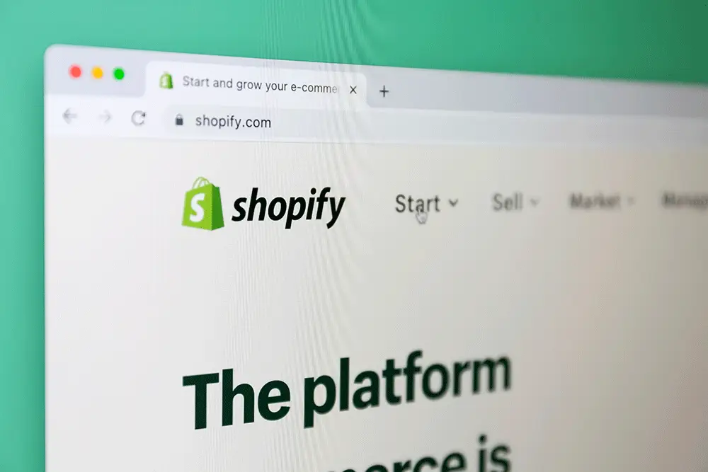 Close-up photo of a computer screen angled to show the shopify.com homepage, its green shopping-bag logo and the headline "The platform"
