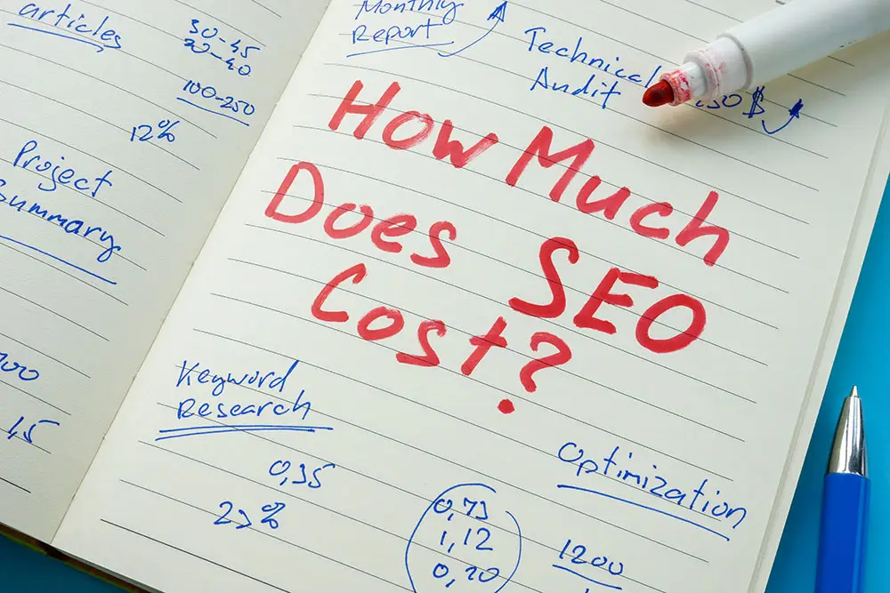 Open notebook with "How Much Does SEO Cost?" in red marker among blue handwritten notes on keyword research, technical audit and optimization.